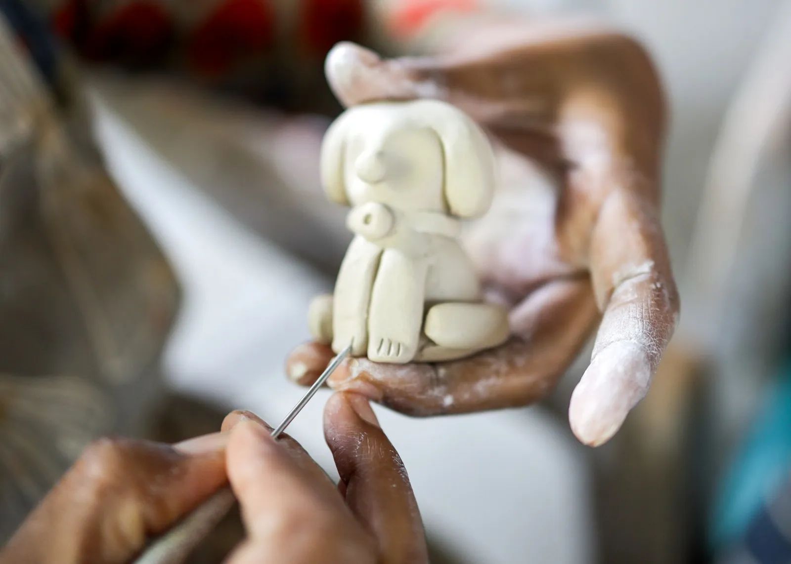 Hands detailing a small clay dog figurine with a needle tool