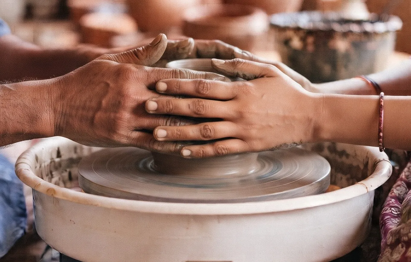 A learner's hands guided by an experienced potter's hands, shaping clay on a pottery wheel